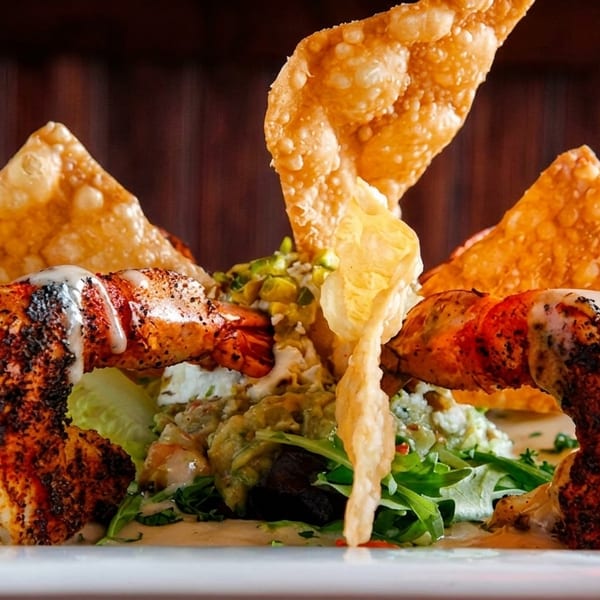 Grilled shrimp with salad, guacamole, cheese, and crispy wonton chips on a white plate.